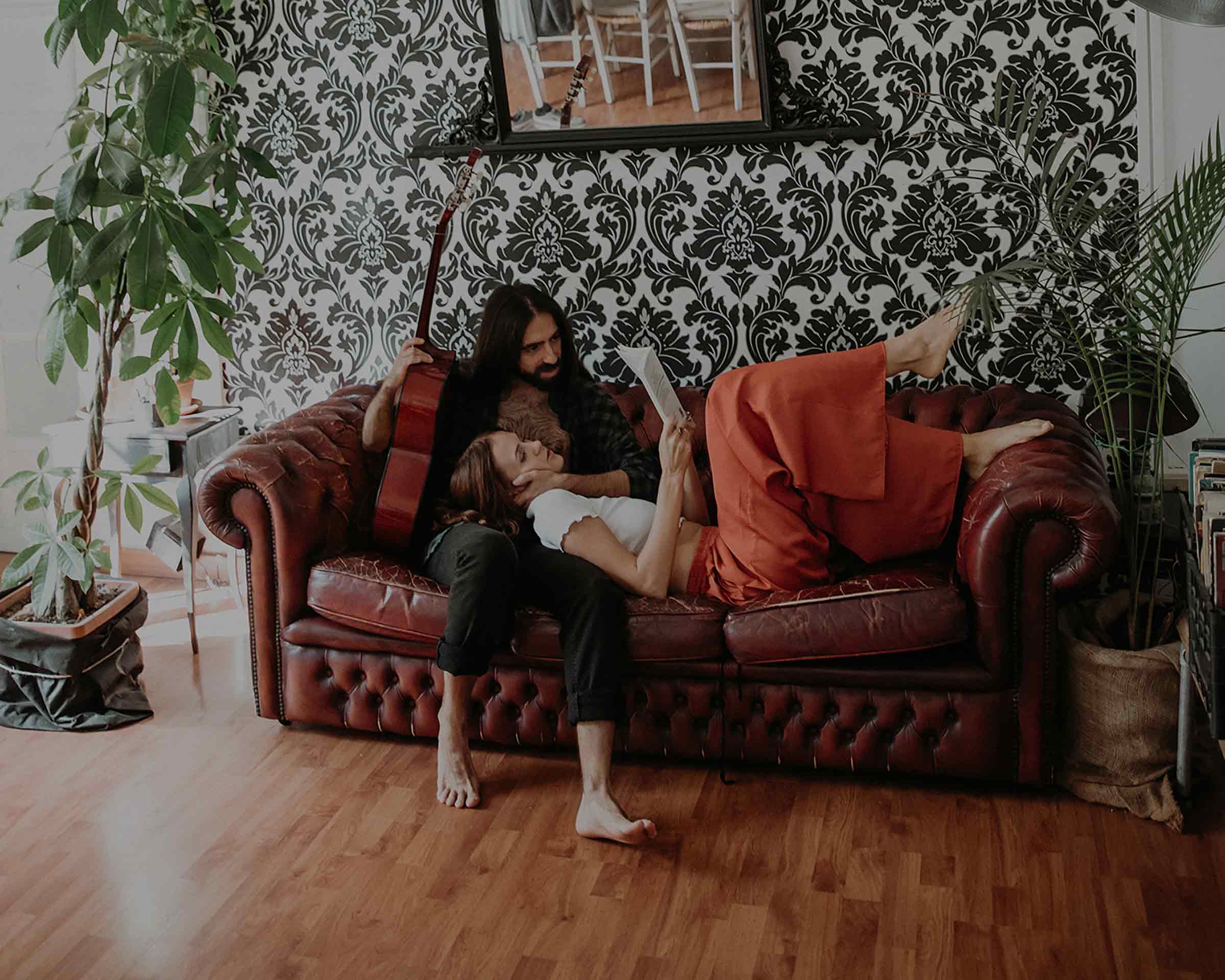 Two residents resting on the red chesterfield in front of the damask wallpaper